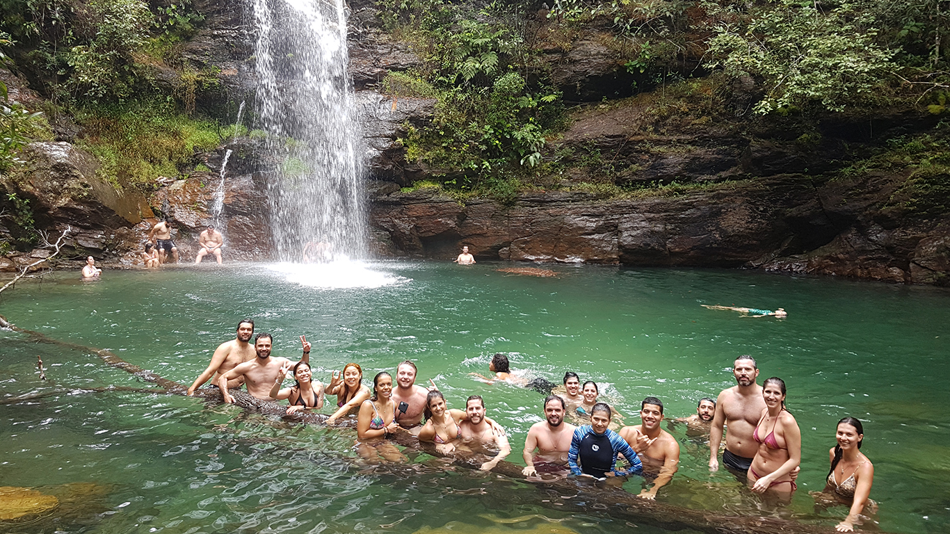 Grupo de turistas posando para foto em cima de uma árvore no poço da cachoeira Santa Bárbara